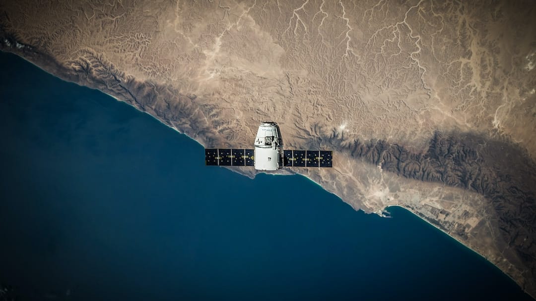 dragon capsule A view of the Dragon 1 space capsule from above as it passes over a coastline on the Earth, far below.